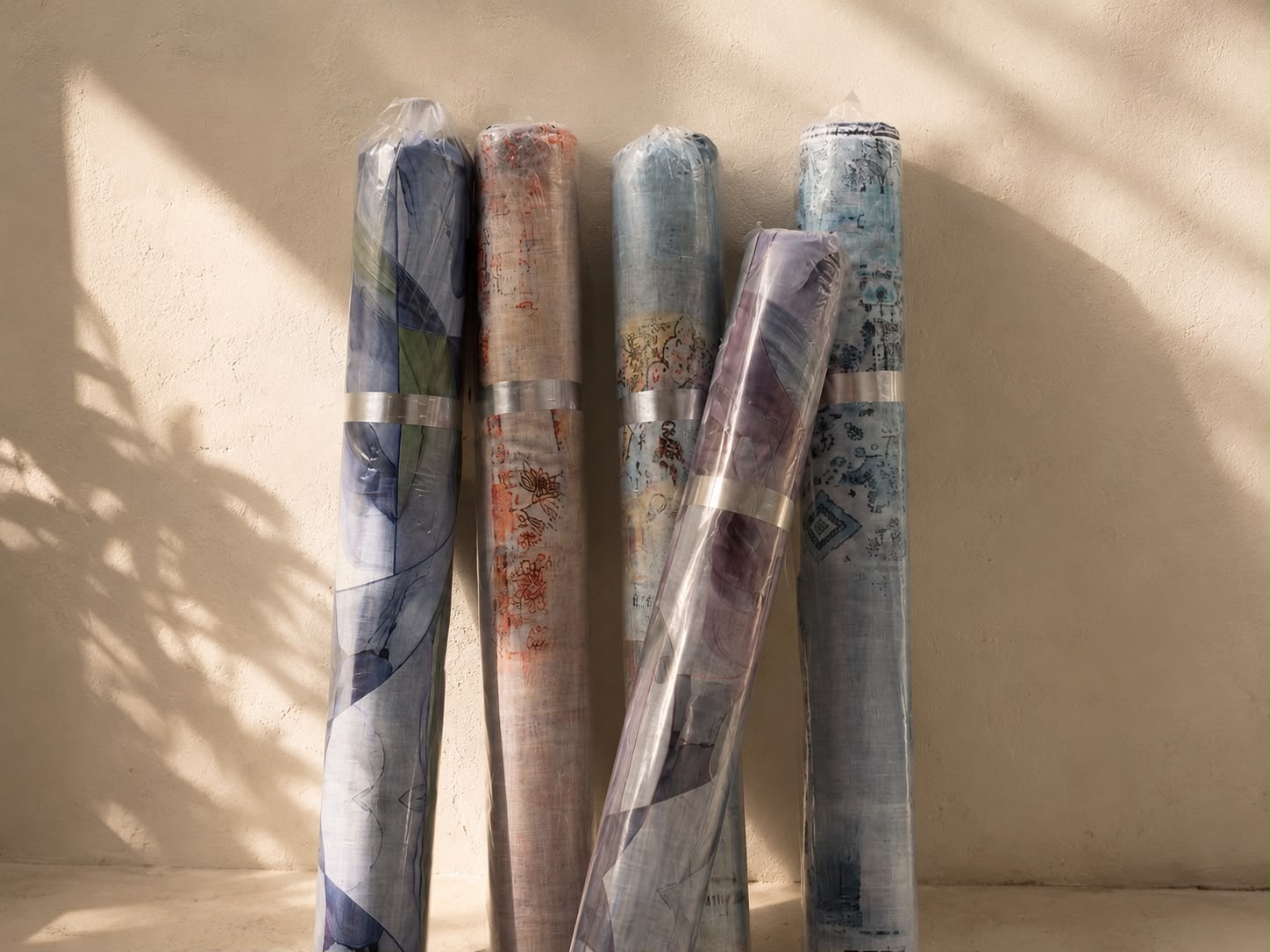 Rolls of printed jacquard and specialty export fabric wrapped and resting against a sunlit mill wall
